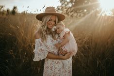 a woman holding a child in her arms while standing in a field with tall grass