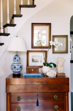 a wooden dresser topped with vases and flowers next to a stair case filled with framed pictures