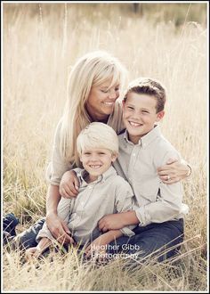 a woman and two boys are sitting in the tall grass with their arms around each other