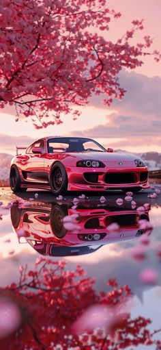 a red sports car parked in front of a tree with pink flowers on it's branches