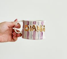 a hand holding a coffee mug with the word dana on it's side, in gold lettering