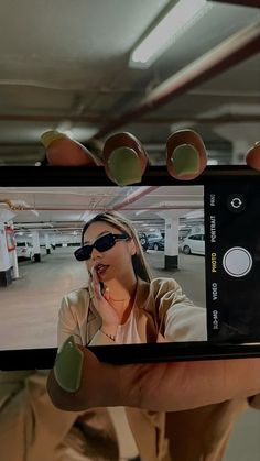 a woman taking a selfie with her cell phone in a parking garage while wearing sunglasses