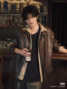 a young man holding a bottle of beer in his hand while standing next to a bar