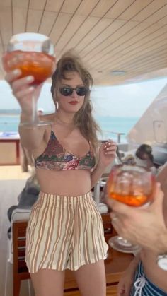 two women in swimsuits holding up drinks on a boat with the ocean in the background