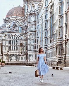 a woman in a blue dress is walking down the street with birds flying around her