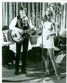 a man standing next to a woman holding a guitar in front of a microphone on stage