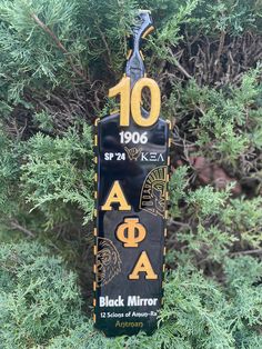 a black mirror hanging from the side of a tree with yellow letters and symbols on it