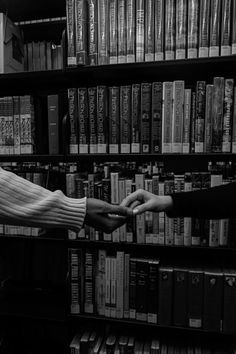 two people reaching out their hands to each other in front of a bookshelf