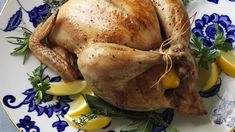 a whole chicken on a blue and white plate with lemons, parsley and herbs