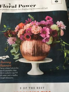 a vase filled with lots of flowers on top of a white cake plate and surrounded by greenery