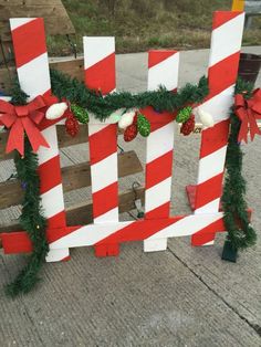 a wooden fence decorated with red and white striped christmas garlands, bows and poinsettis