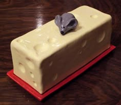 a square cake with white frosting and a gray mouse on top, sitting on a red plate