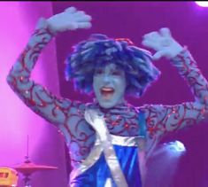 a woman dressed in blue and white dancing on stage with her hands up to the side