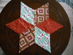 a wooden table topped with a brown plate covered in quilts and star shaped pieces