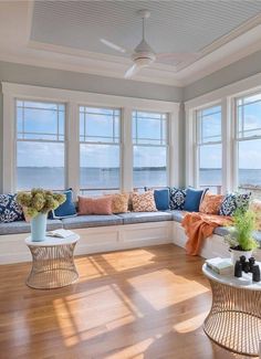 a living room filled with lots of windows and furniture next to the ocean on top of a hard wood floor