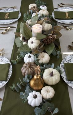 the table is set with white pumpkins and greenery, gold gourds