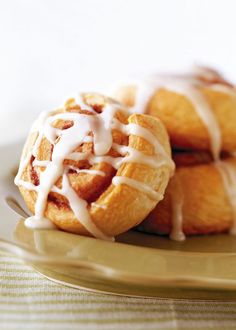 three cinnamon rolls on a plate with icing drizzled over them and sitting next to each other