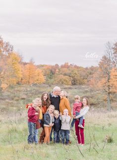 a family poses for a photo in an open field with fall foliage and trees behind them