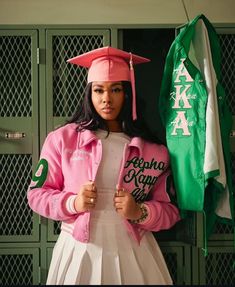 a woman in a pink and white graduation outfit holding a green jacket with the words south africa on it