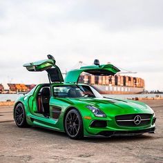 a green sports car with open doors parked in front of a large cargo ship on the water