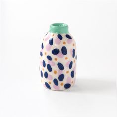 a ceramic vase with multicolored polka dots on the outside and green top, sitting against a white background