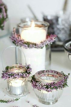 three glass jars with flowers on them sitting next to each other and one candle in the middle