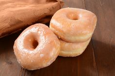 three glazed donuts sitting on top of a wooden table next to a brown bag