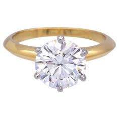 a yellow gold ring with a round brilliant cut diamond in the center, on a white background