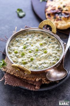 a bowl of soup on a plate with a spoon and some bread in the background