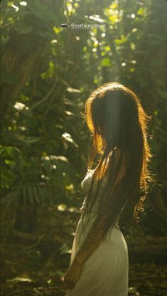 a woman with long hair standing in front of trees and sunlight shining through the leaves