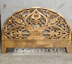 a gold metal headboard sitting on top of a cement floor next to a wall