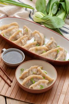 some dumplings are sitting on a plate with dipping sauce and chopsticks next to them