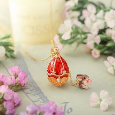 a small red and gold egg shaped pendant next to pink flowers