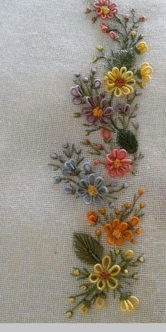 an embroidered piece of cloth with flowers and leaves on the side, in various colors