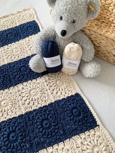 a teddy bear sitting on top of a blue and white rug next to a ball of yarn