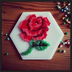 a red rose made out of legos sitting on top of a table next to beads