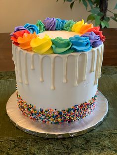 a white cake with rainbow frosting and sprinkles on the top is sitting on a table