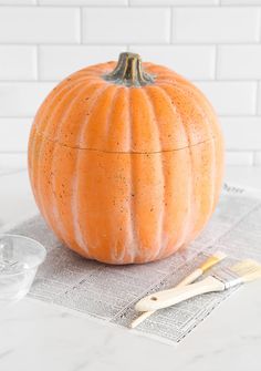 an orange pumpkin sitting on top of a newspaper next to a cup and spoons