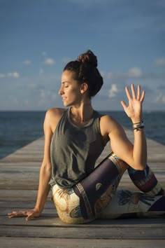 a woman is sitting on the dock doing yoga exercises with her hands in the air