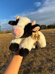 a hand holding a small stuffed cow with the word ab on it