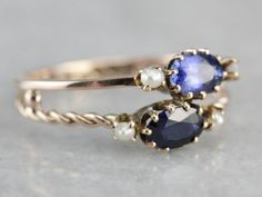 "Two bands, one twisted, one simple and polished have been fused together to create this ready-made stacking set, with oval cut sapphires, one a shade darker than the other, both accented perfectly by creamy white seed pearls, this ring is wonderfully crafted, unique and super sweet! Metal: 10K Yellow Gold Gem: 2 Sapphires totaling 1.11 Carats Gem Measurements: 6 x 4 mm, Oval Accents: 4 Seed Pearls Ring Size: 8.25 Marks: \"10K\" Stamped on the inside band SKU #: U52URV7Y Each piece has been iden Elegant Stackable Sapphire Rings With Rose Cut Diamonds, Modern Twist Oval Ring For Formal Occasions, Heirloom Oval Stackable Jewelry, Elegant Oval Multi-stone Stackable Rings, Oval Jewelry With A Modern Twist For Weddings, Modern Twist Oval Wedding Jewelry, Oval Gemstone Stackable Rings For Formal Occasions, Formal Oval Gemstone Stackable Rings, Modern Twist Oval Rings For Anniversary