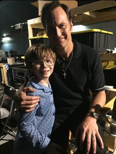 a man sitting next to a little boy on top of a wooden chair in a room