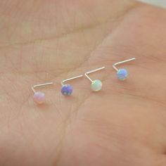 three tiny opal earrings on a person's hand, one is white and the other is blue