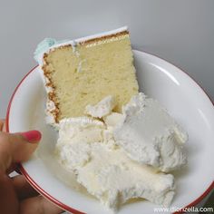 a piece of cake with white frosting on a red and white plate, being held by a hand