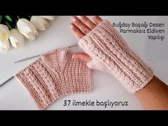 a hand holding a pair of knitted fingerless mitts next to a white flower