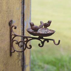 a metal bird feeder hanging from the side of a wooden door with green grass in the background