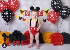 a baby in mickey mouse costume standing next to balloons