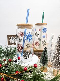 two cups with straws are sitting next to christmas trees