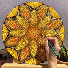 a hand holding a pencil and drawing on a yellow flower shaped plate with orange petals