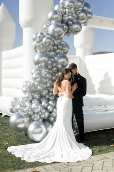 a bride and groom standing in front of a large sculpture with silver balls on it